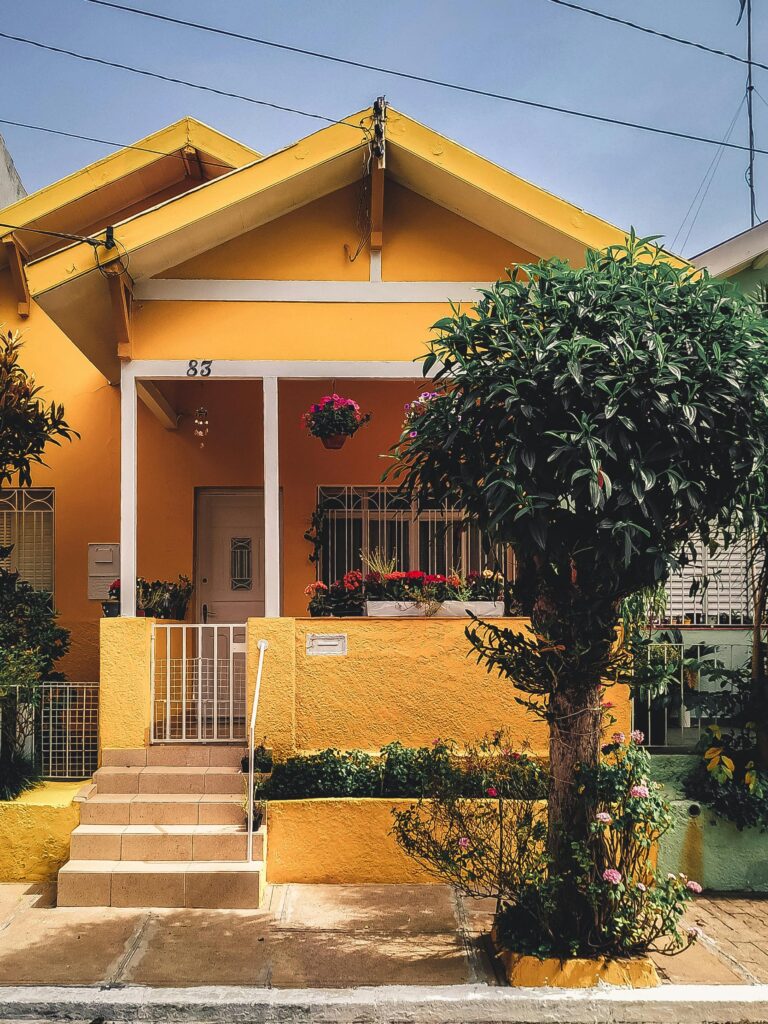 pexels-photo-2102587-2102587 Bright yellow house with lush garden, vibrant flowers, and welcoming porch entrance.
